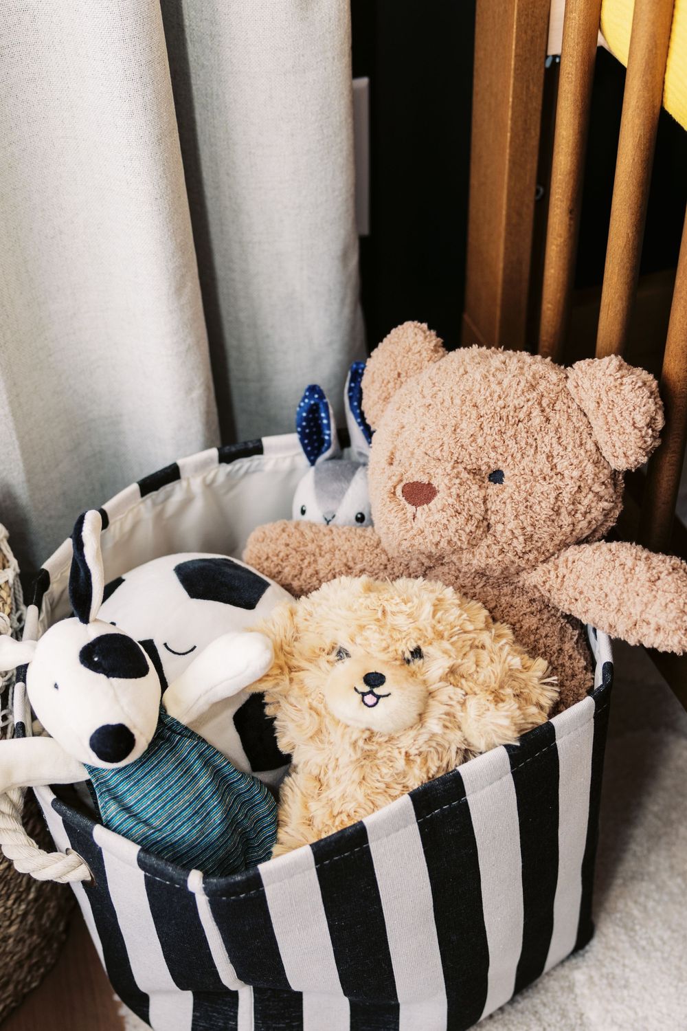 Black and white striped storage basket filled with plush stuffed animals including a teddy bear in a nursery.