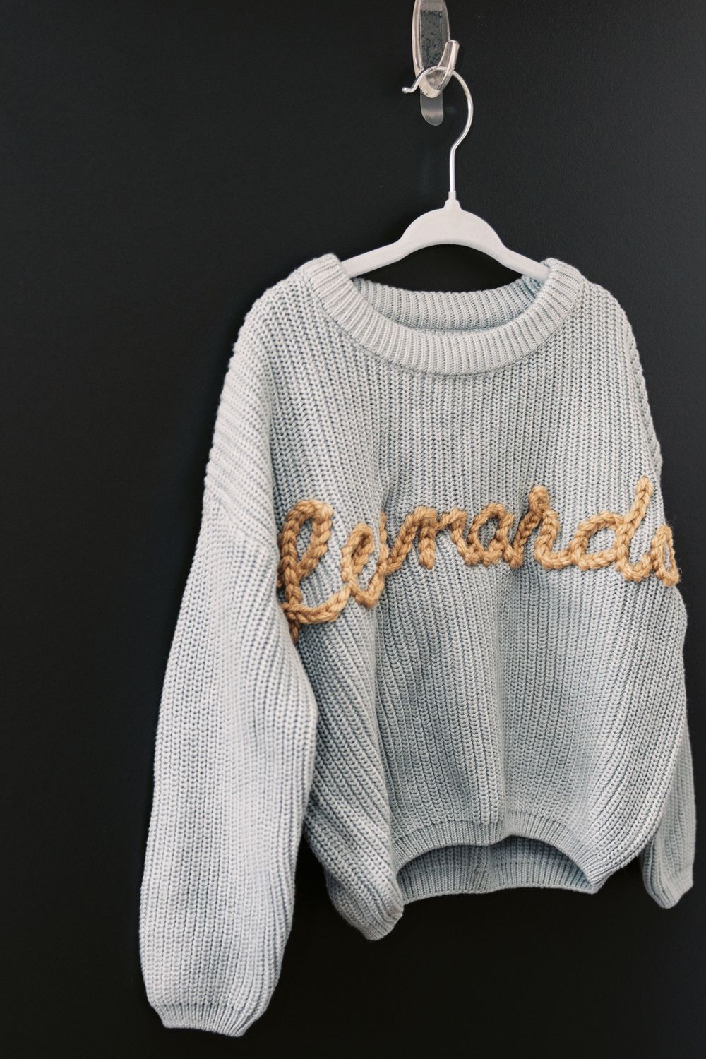Light blue chunky knit personalized baby sweater with gold Leonardo name embroidery hanging on white hanger.