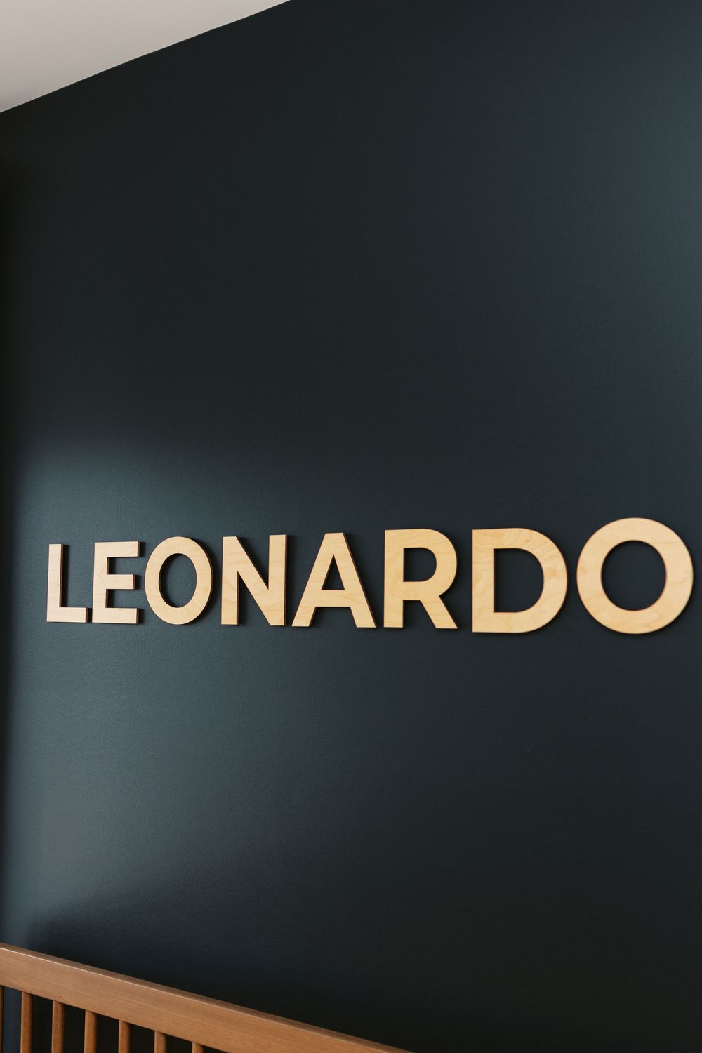 Gold LEONARDO name letters mounted on dark navy accent wall in a stylish modern nursery room.