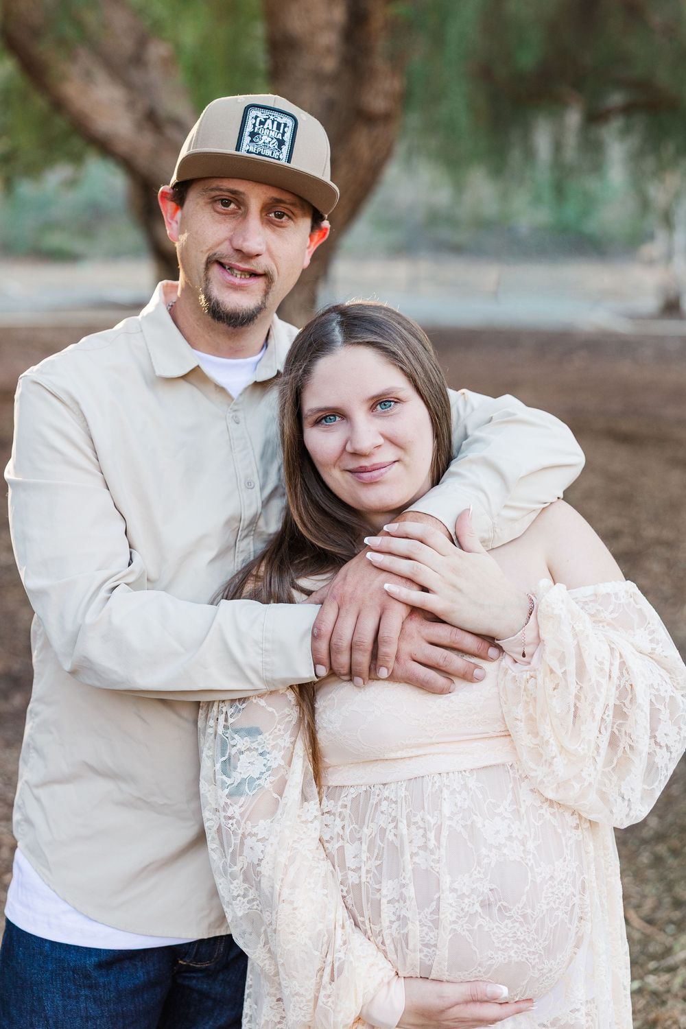 A couple embraces outdoors in a romantic photoshoot series wearing cream and white tones against a natural backdrop.