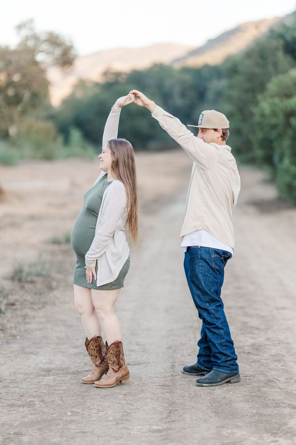A couple in western attire dancing together on a dusty trail at sunset, with cowboy boots and jeans.