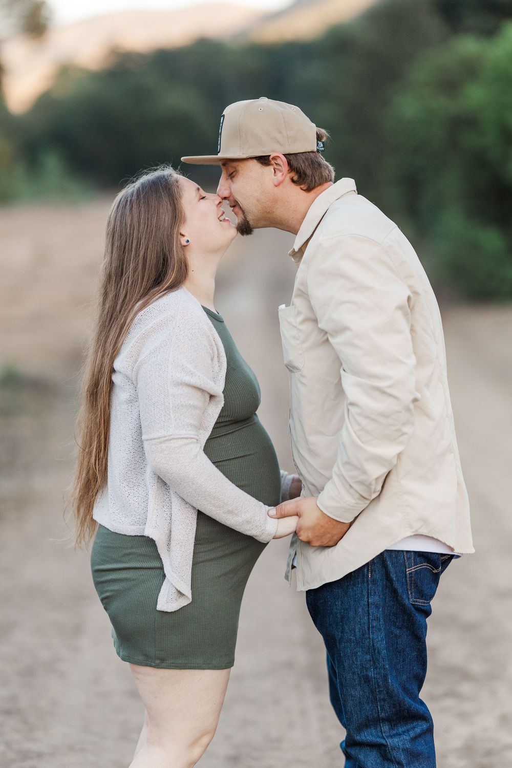 A couple shares intimate moments during an outdoor maternity photoshoot in casual attire.