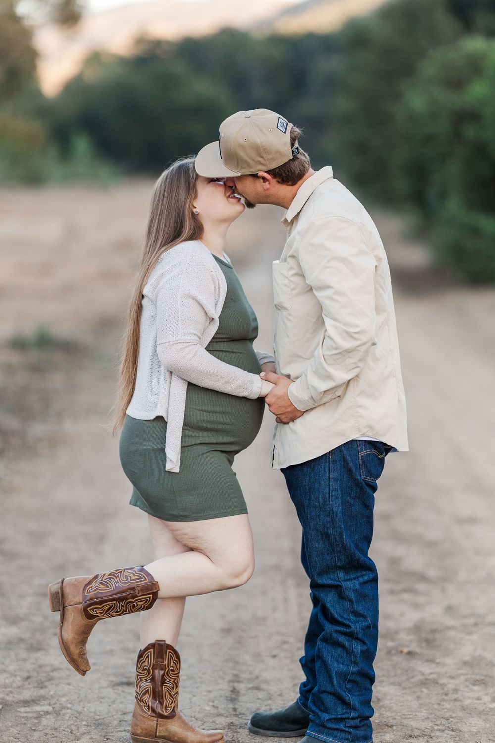 Romantic maternity photo of couple embracing on dirt path with mountains in background.
