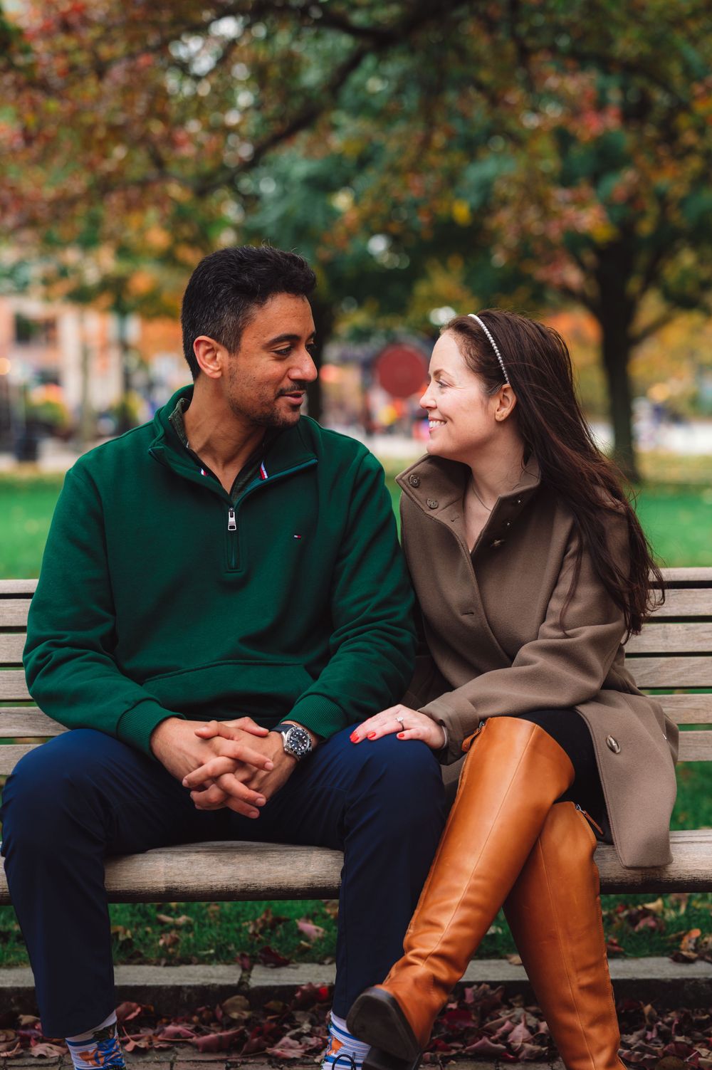 Couple sitting close together on park bench surrounded by autumn leaves.