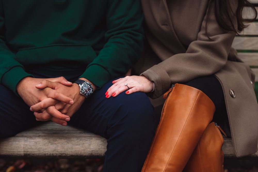 Close-up of hands resting on lap showing brown boots and casual attire.