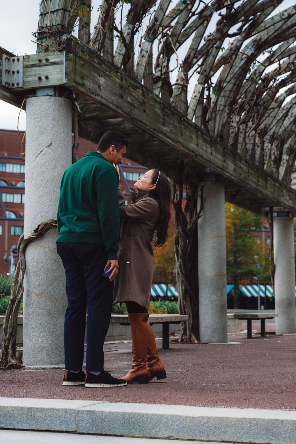 Couple sharing an intimate moment under a decorative wooden archway in an urban park.