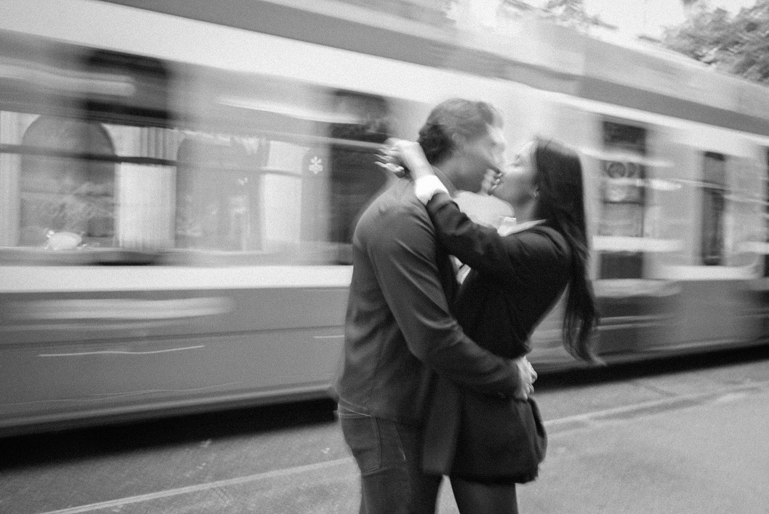 A black and white sequence of photos showing two people embracing and kissing on a train platform as trains pass by.