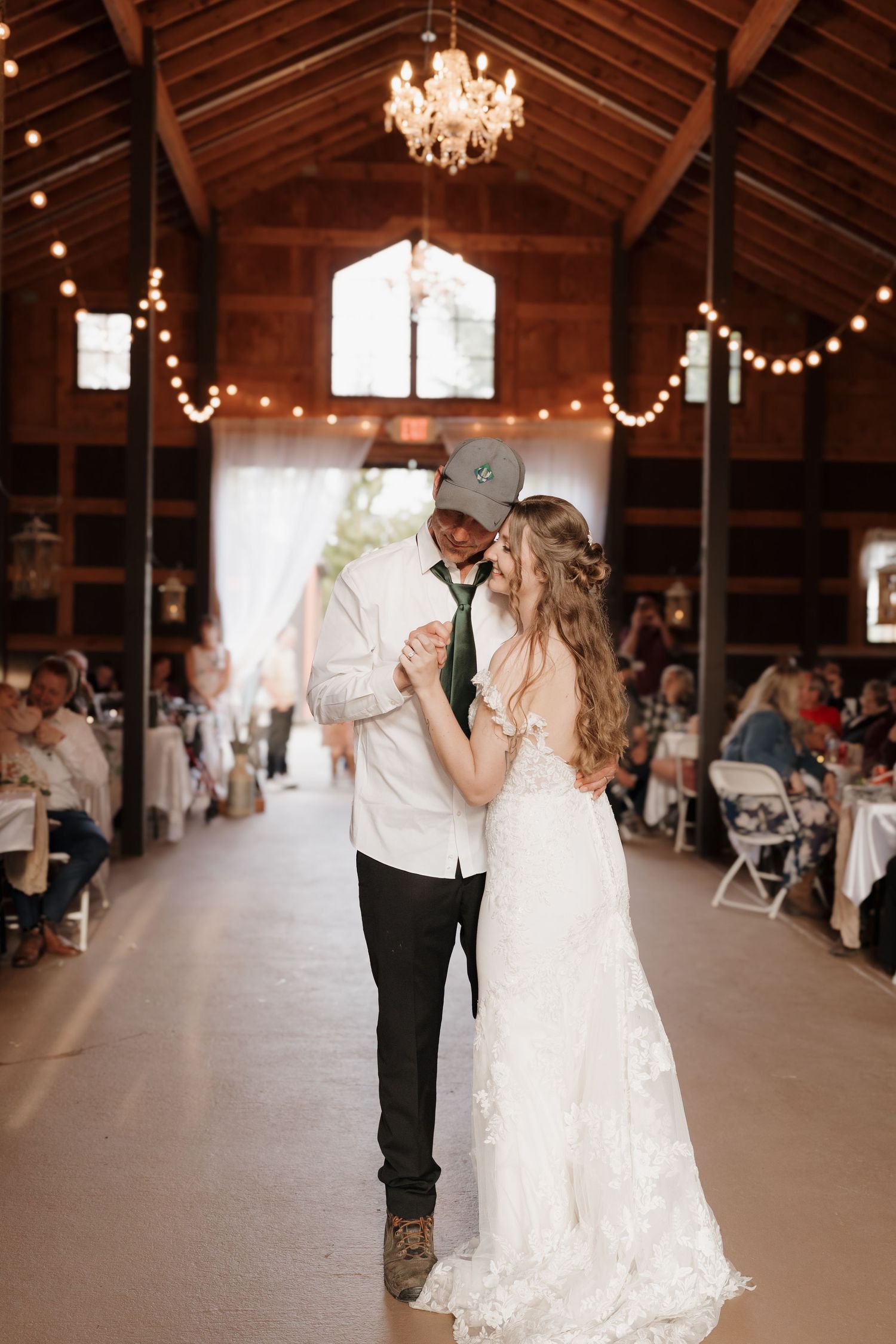 A couple shares their first dance in a rustic barn venue decorated with chandeliers and string lights. Leavenworth, WA