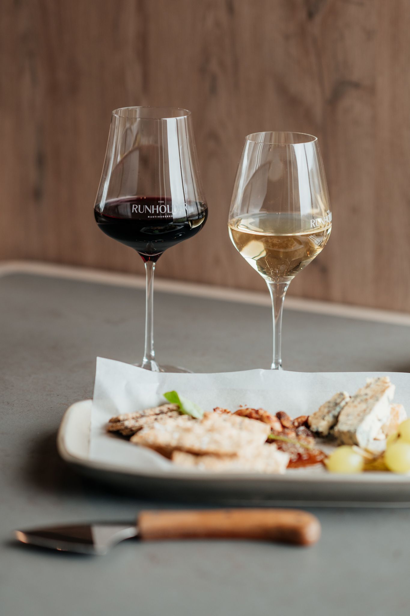 Wine glasses filled with red and white wine sit alongside elegant plated dishes on a table at the Runholder by August and Vine