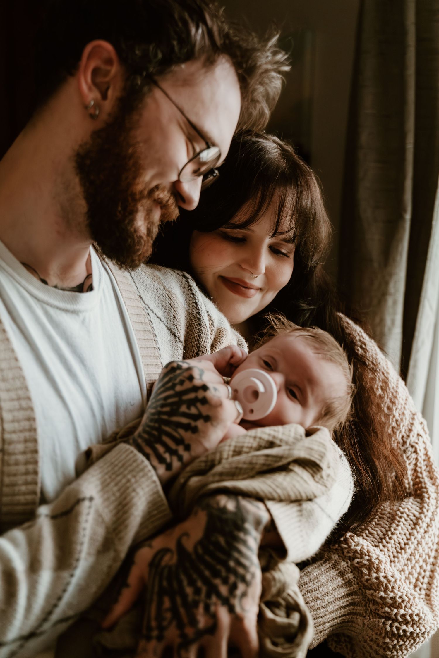 New parents tenderly cradling their newborn baby with a pacifier in a warm cozy home setting.