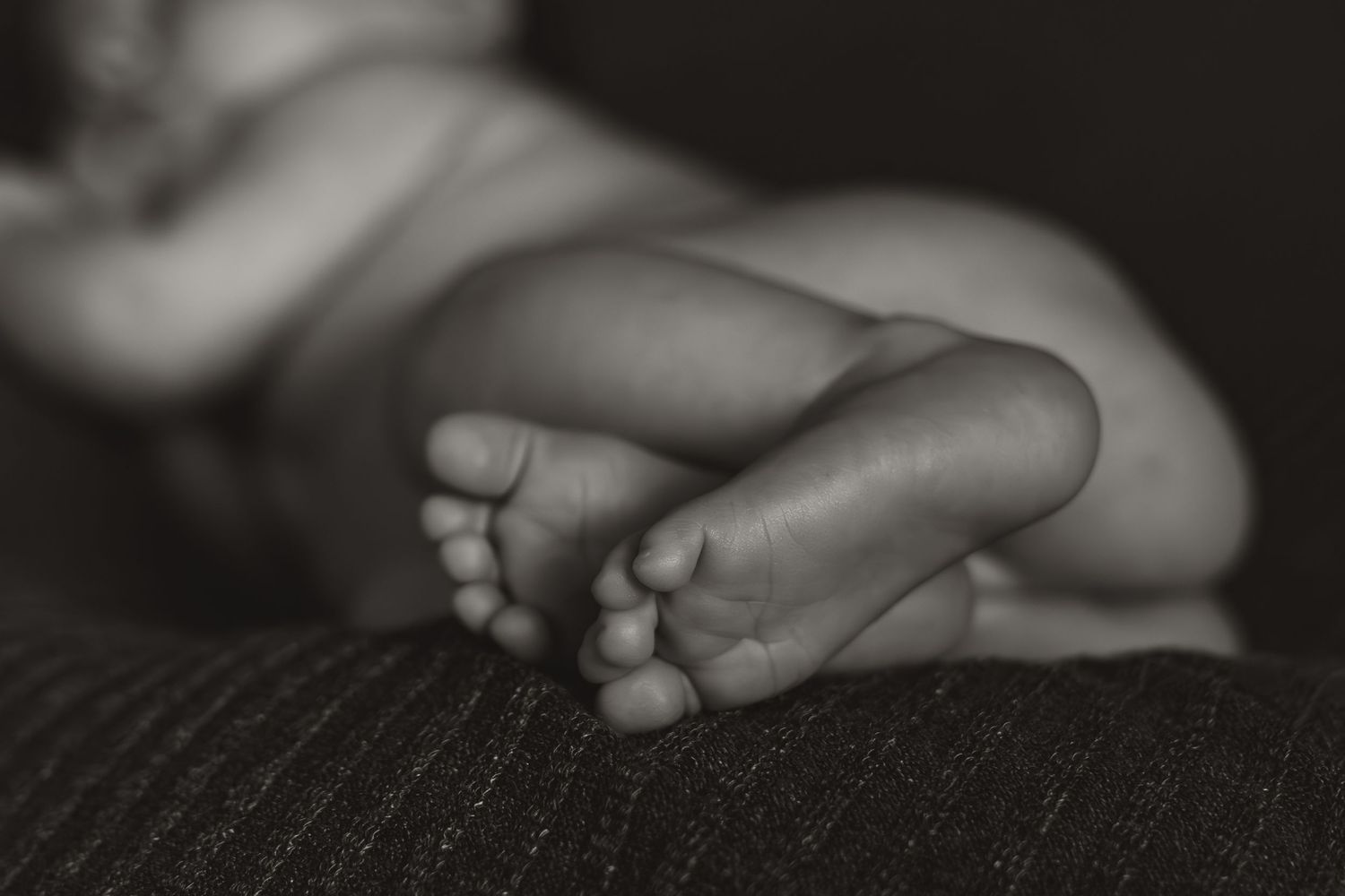 Close-up black and white photo of tiny newborn baby feet crossed together on a textured blanket.