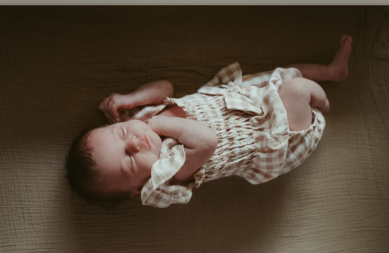 Sleeping newborn baby in a white checkered romper lying on a wooden floor from above.