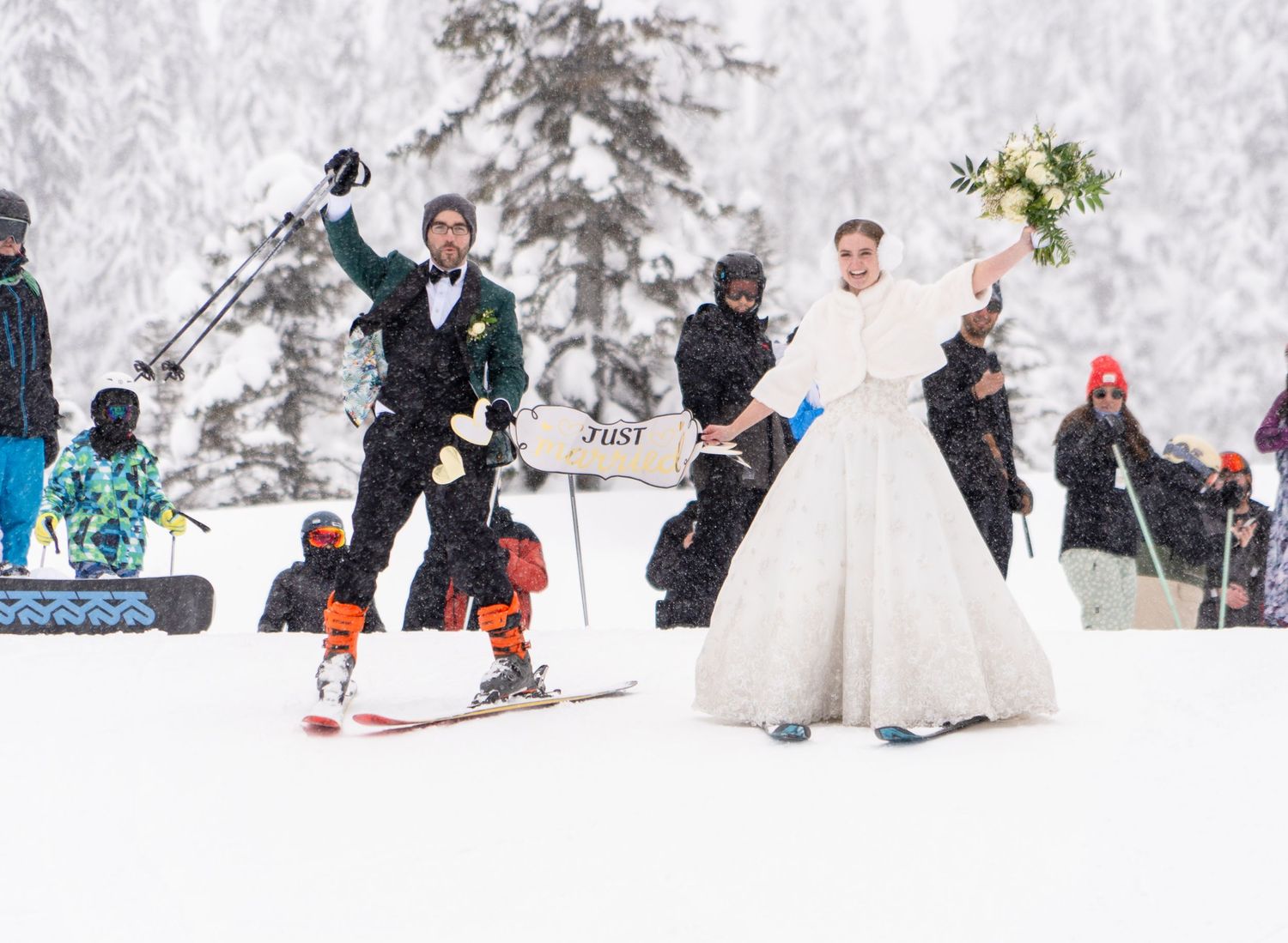 A wedding celebration on ski slopes with people skiing in formal attire among snow-covered trees.