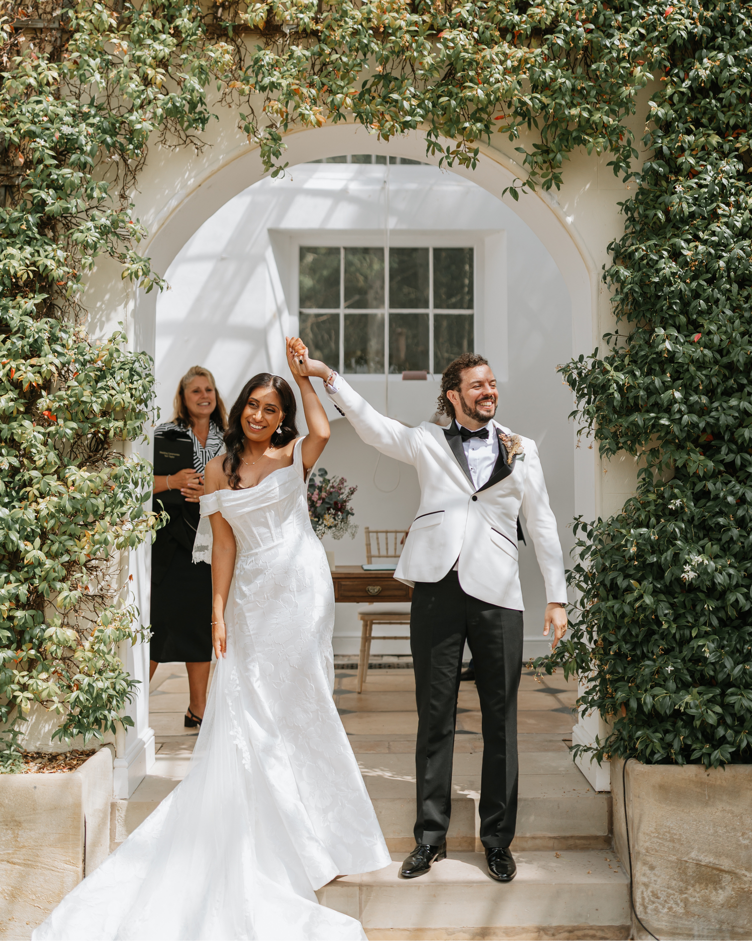 A wedding party dances and celebrates in a sequence of candid moments under an elegant white archway with greenery.