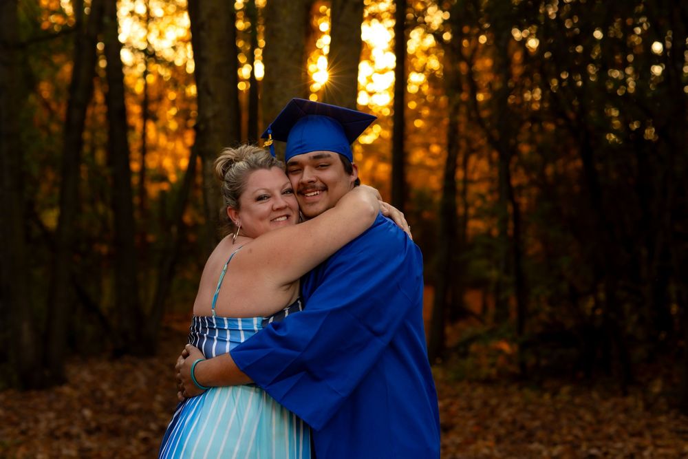 A couple embraces in a wooded area during golden hour as sunlight filters through autumn trees.