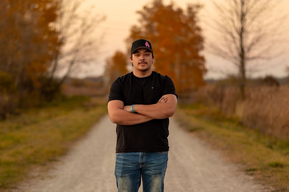 A person in a black t-shirt and jeans stands on a gravel path surrounded by autumn foliage.