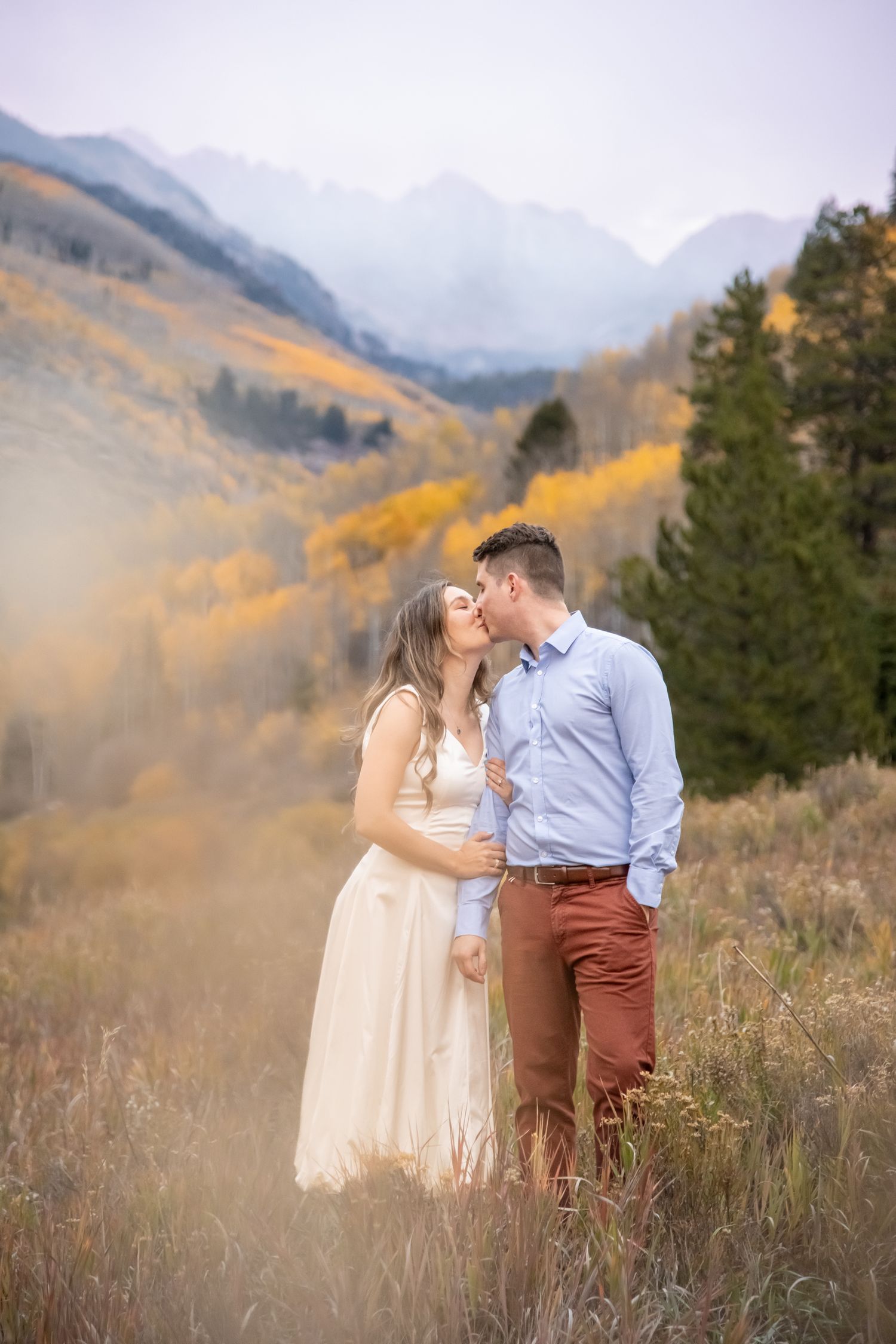 A couple shares a tender moment in a mountain meadow with golden autumn foliage and misty peaks in the background engagement photos in Vail