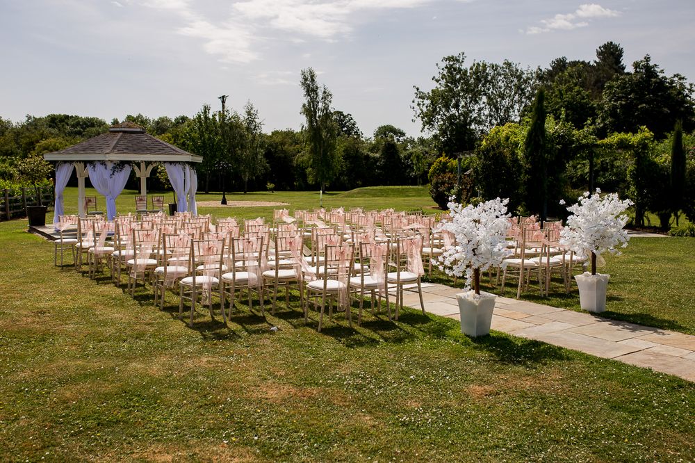Wide angle view of outdoor wedding ceremony setup with decorated chairs and gazebo.
