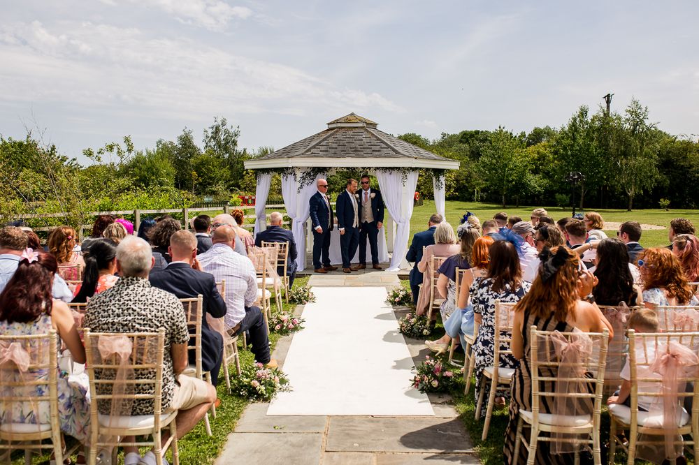 Outdoor wedding ceremony setup with white chairs and fabric draping along a garden path.