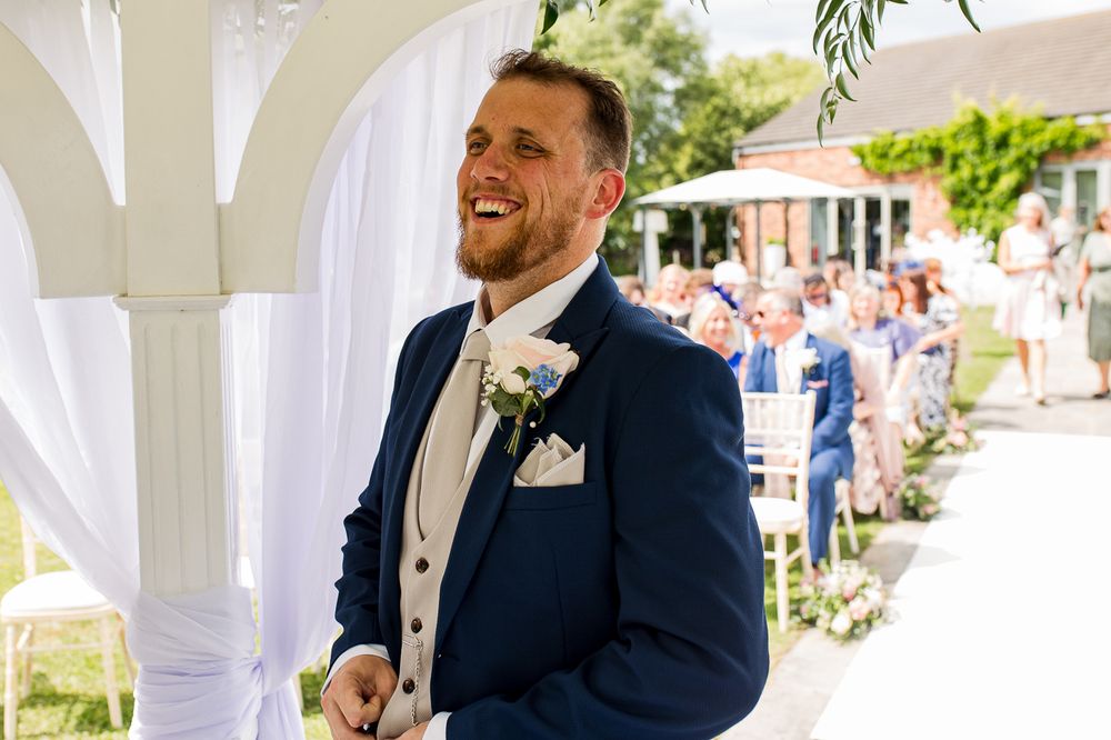 Wedding party members gather under white pergola during outdoor summer celebration.