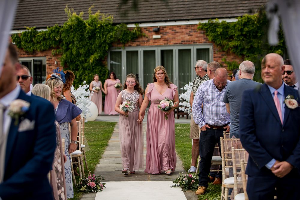 Wedding guests and attendants in formal attire gather outside brick venue building.