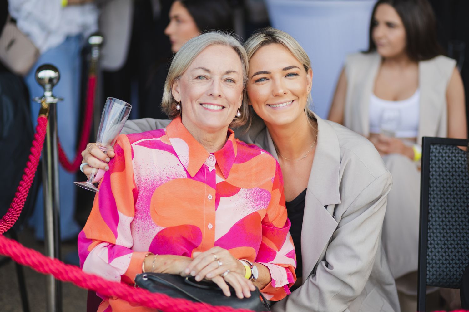 Two women smiling together at an outdoor social event wearing bright floral attire.