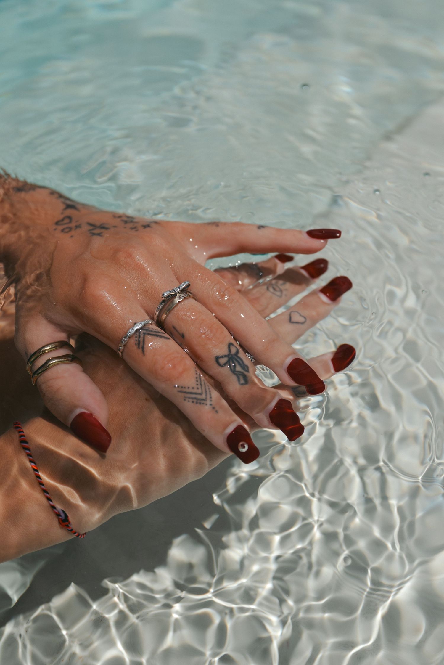 Hand with silver rings and dark nail polish submerged in crystal clear rippling water.