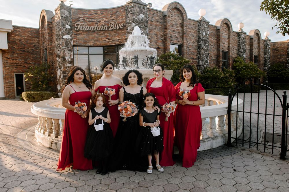Wedding party in red and black attire poses together in front of a historic brick building.