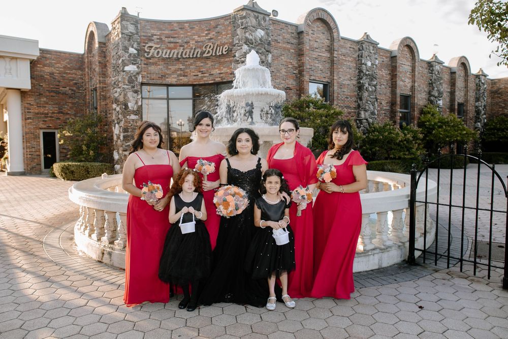 Wedding party members in formal attire pose for photos outside a stone building with white architectural details.