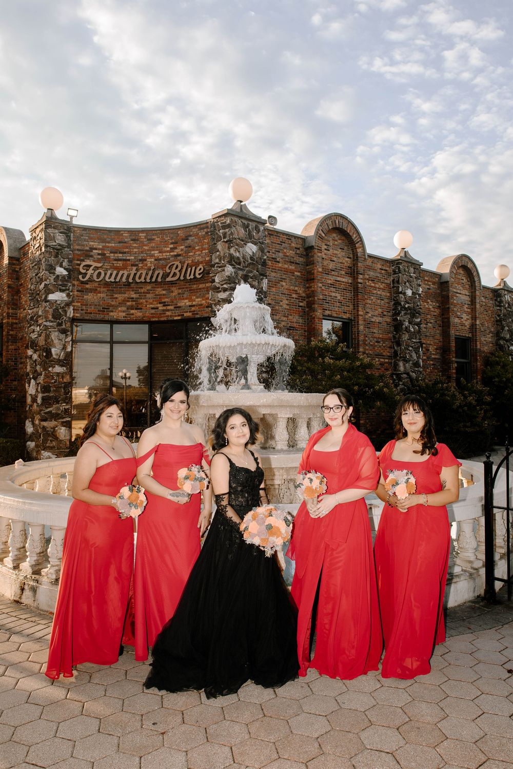Wedding party poses by a fountain at Fountain Blue venue with bridesmaids in red dresses.