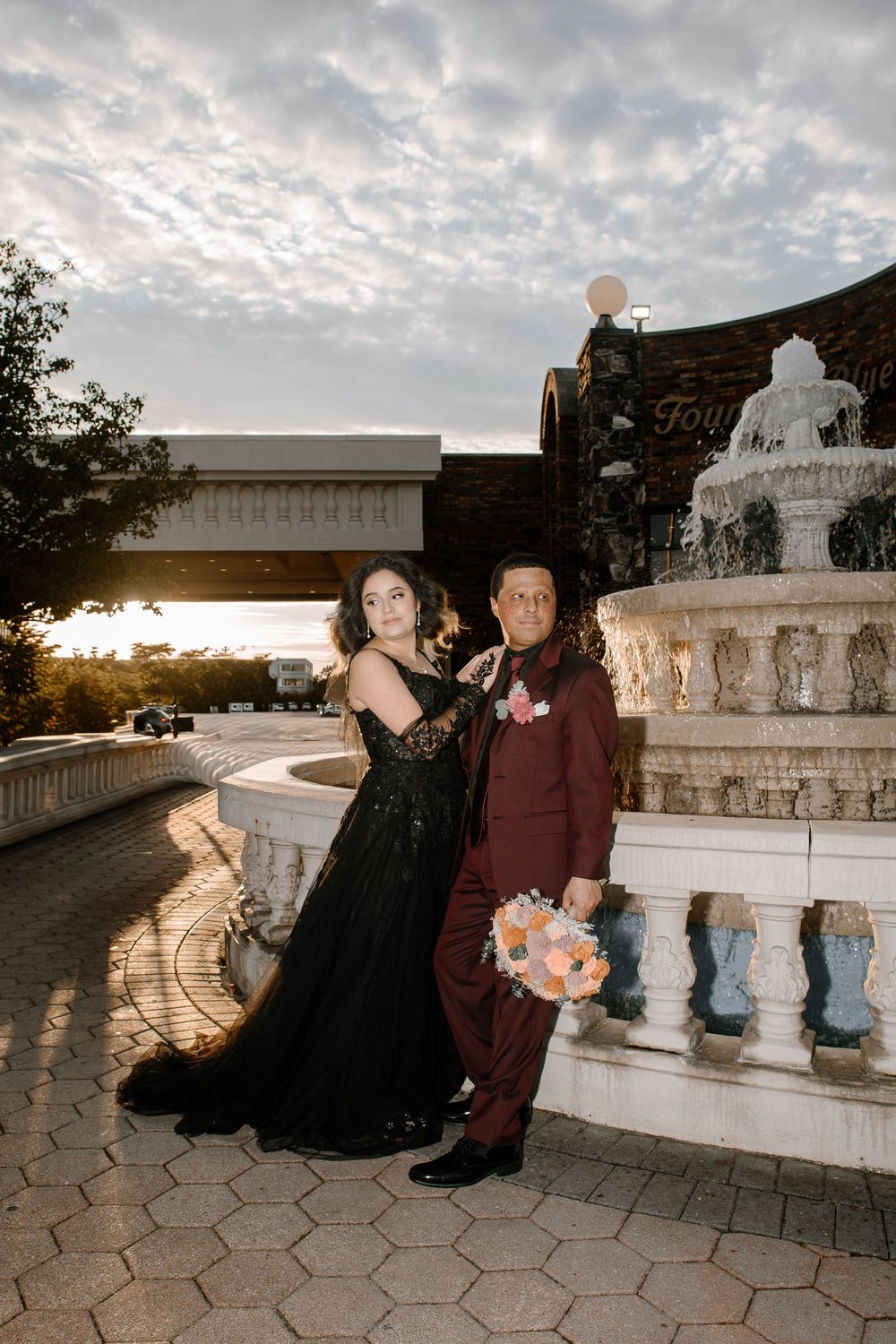 Romantic sunset photos at an ornate stone fountain featuring elegant formal wear and floral bouquet.