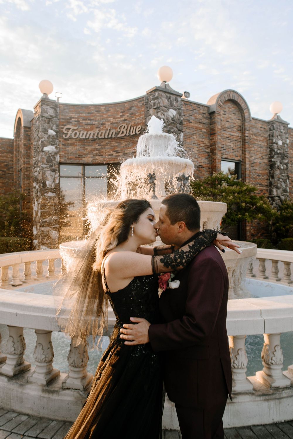 Romantic moment captured at sunset against stone architecture with white balloons floating in background.