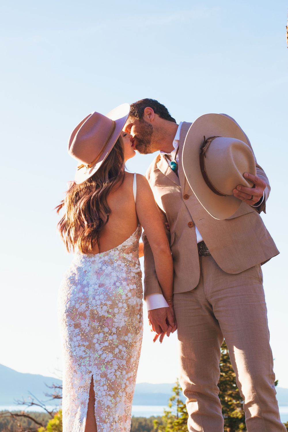 Bride and groom in matching tan cowboy hats sharing a kiss at outdoor wedding.