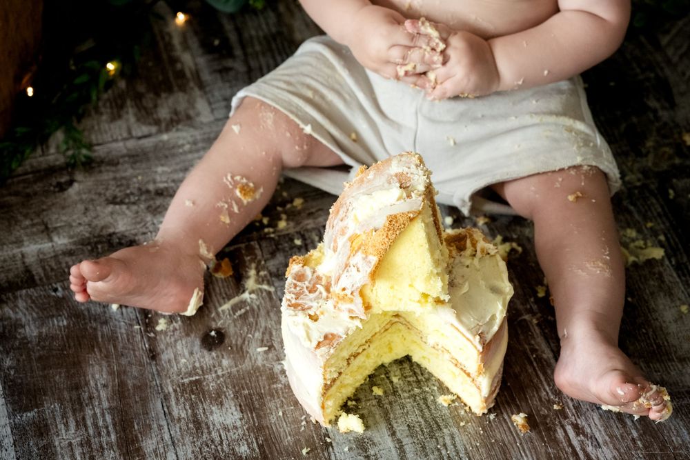 Baby smashing a yellow frosted cake on a wooden surface during a first birthday cake smash photoshoot.