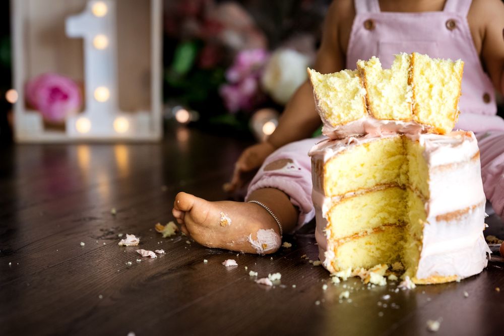 Baby smashing a yellow layered birthday cake with a crown topper on a wooden floor at a first birthday party.