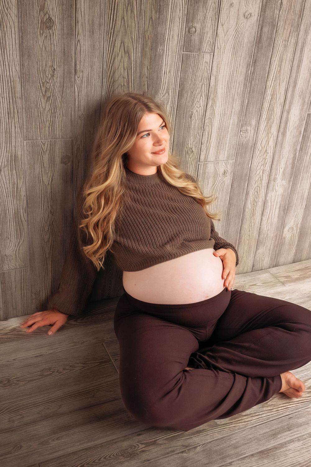 Maternity photo series showing a brown sweater against wooden wall background.