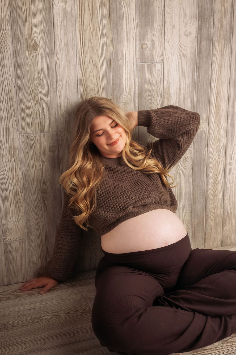 Person wearing brown sweater relaxes against rustic wooden wall in cozy indoor setting.