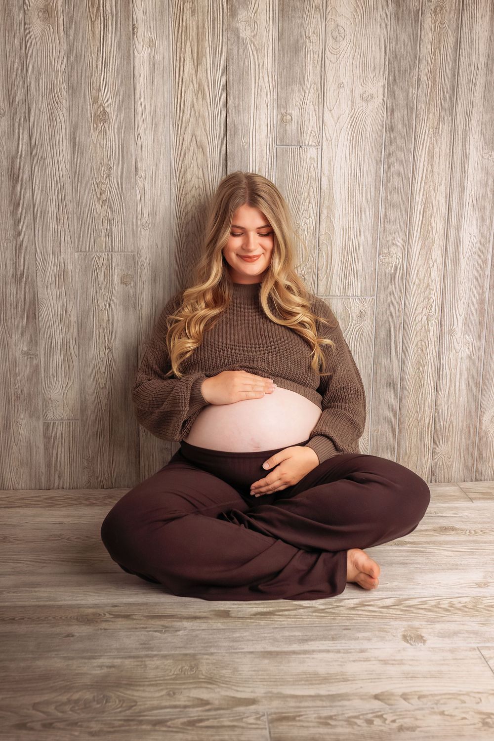 A series of maternity photos showing a pregnant woman in a brown sweater dress posing on a wooden floor.