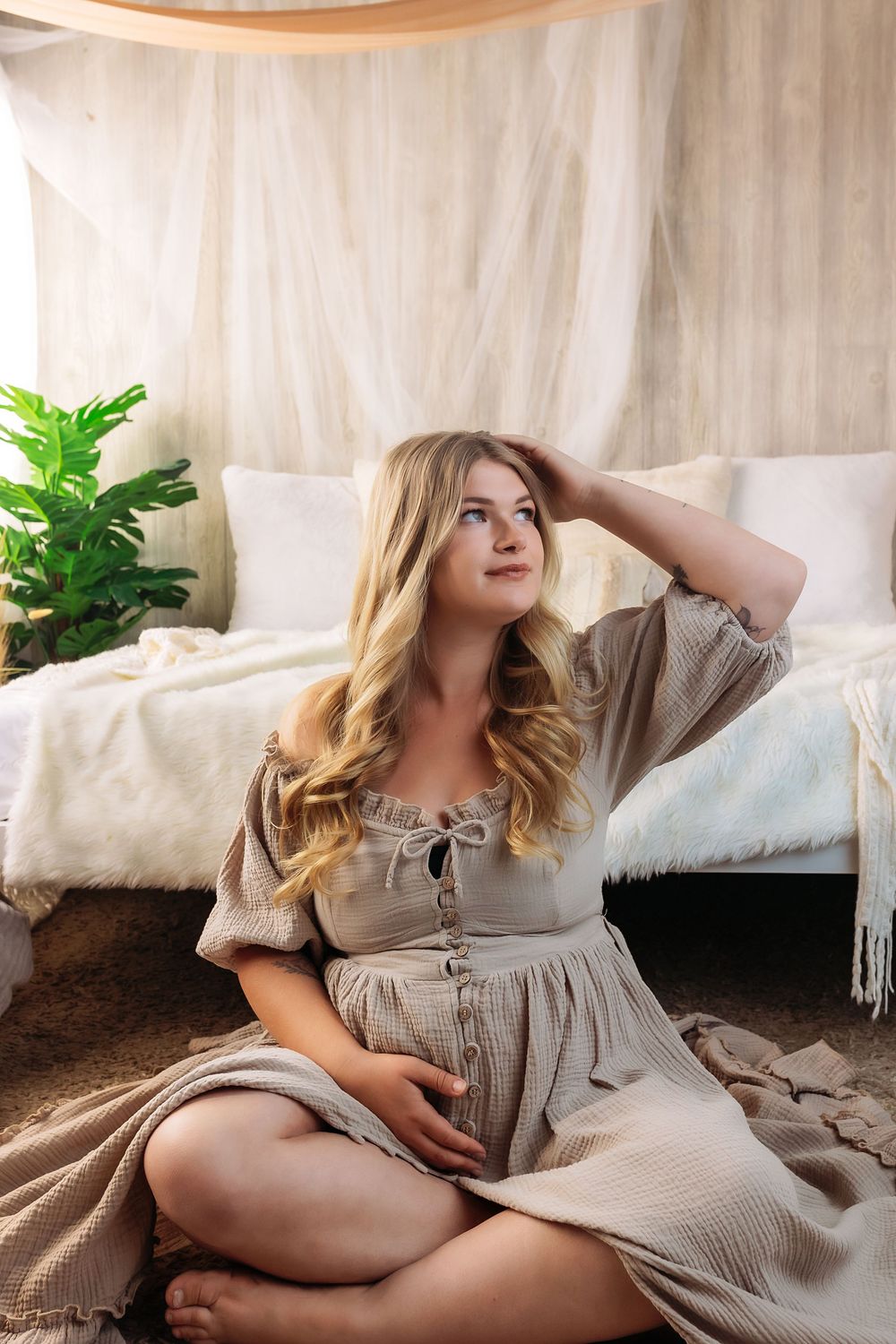 A soft and dreamy boudoir photoshoot featuring a gray dress on a white bed with decorative plants in the background.