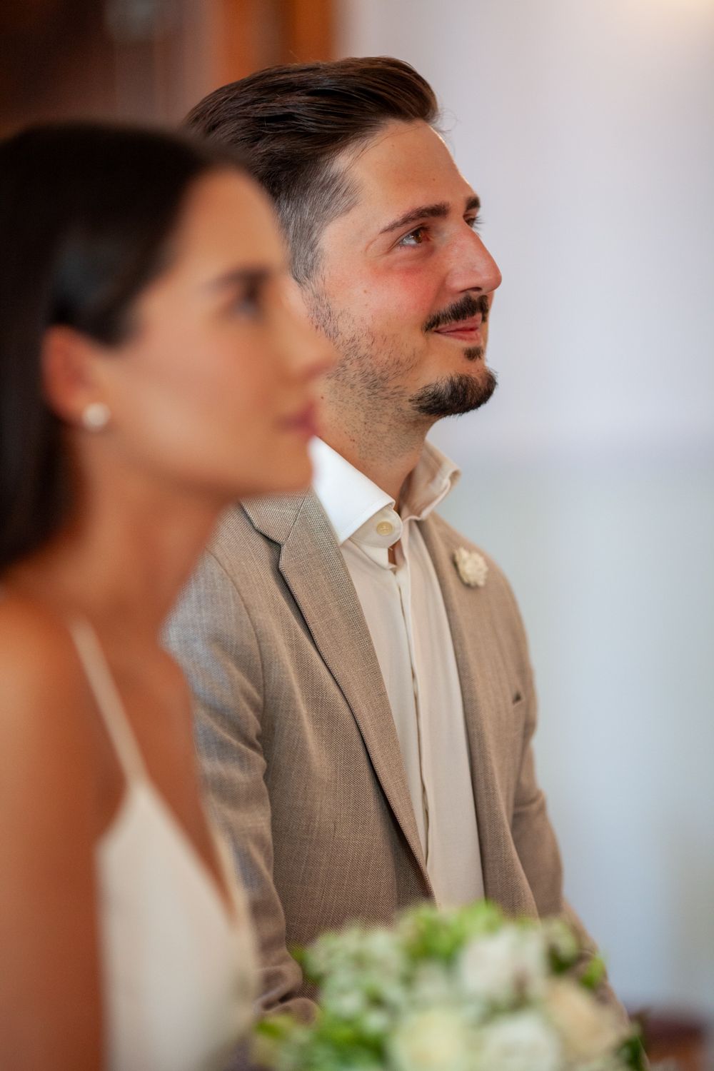 Wedding party members in formal attire sit at a table with floral arrangements.