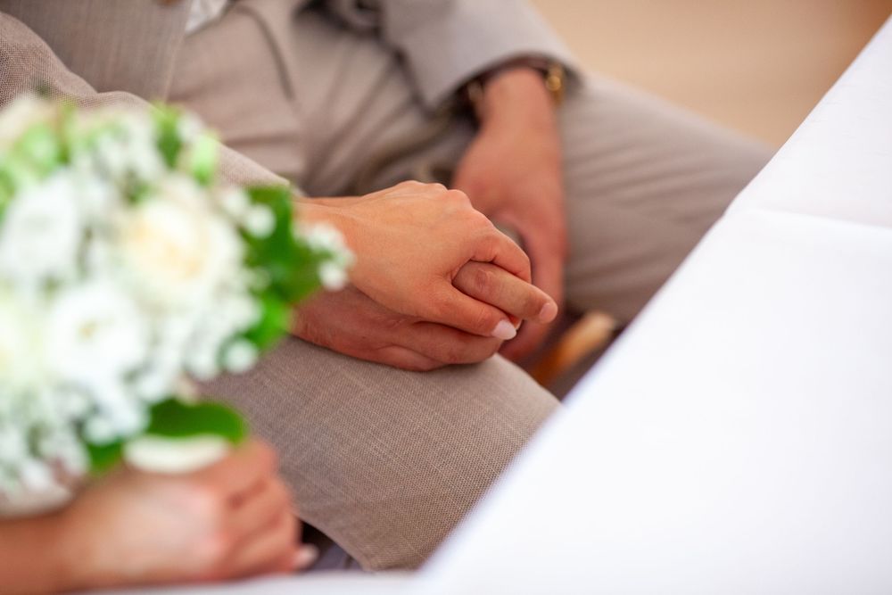 Close-up view of hands holding a delicate white rose corsage against a soft beige background.
