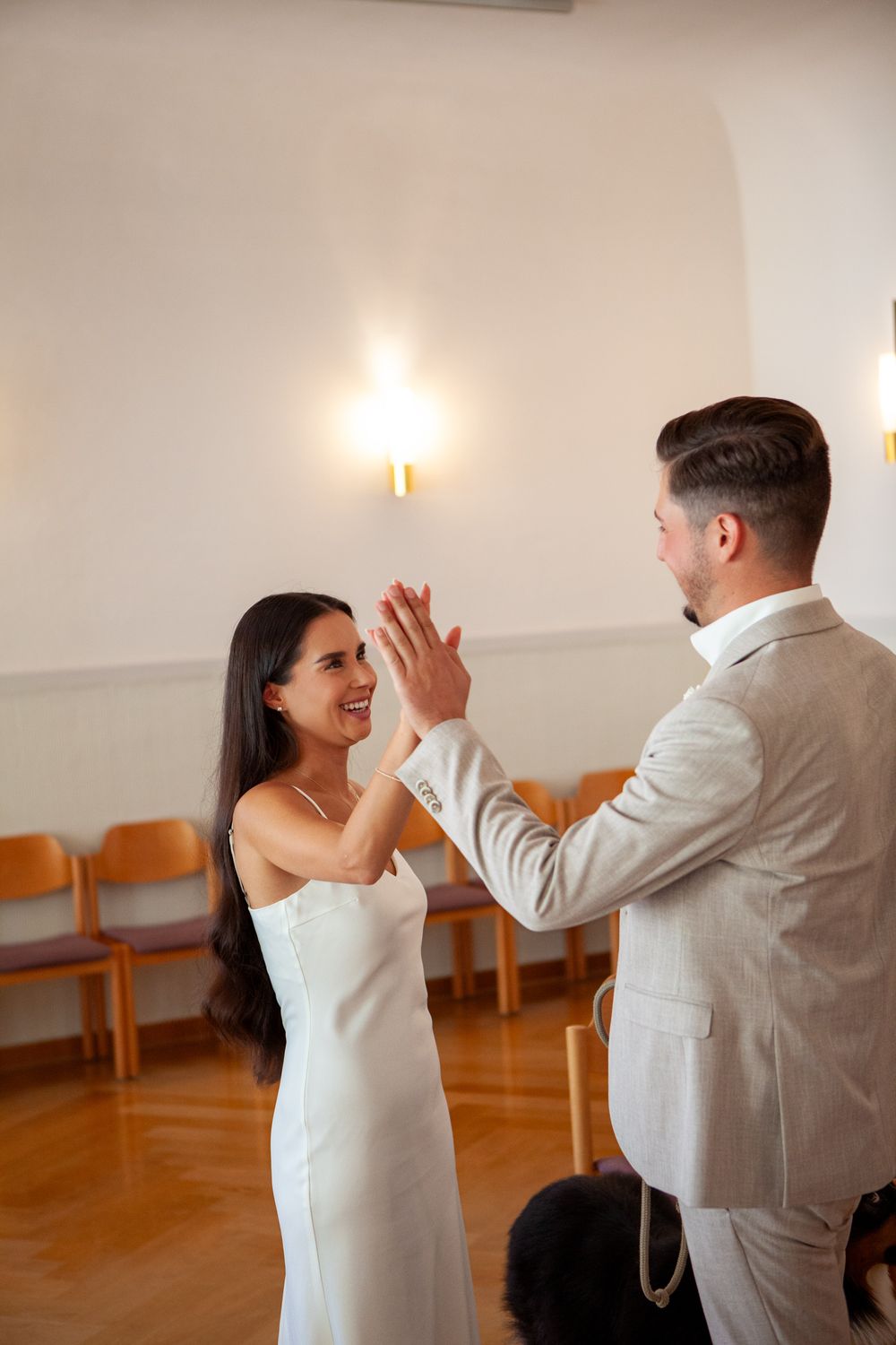 A couple in formal attire sharing a joyful moment together on a dance floor with orange chairs in the background.