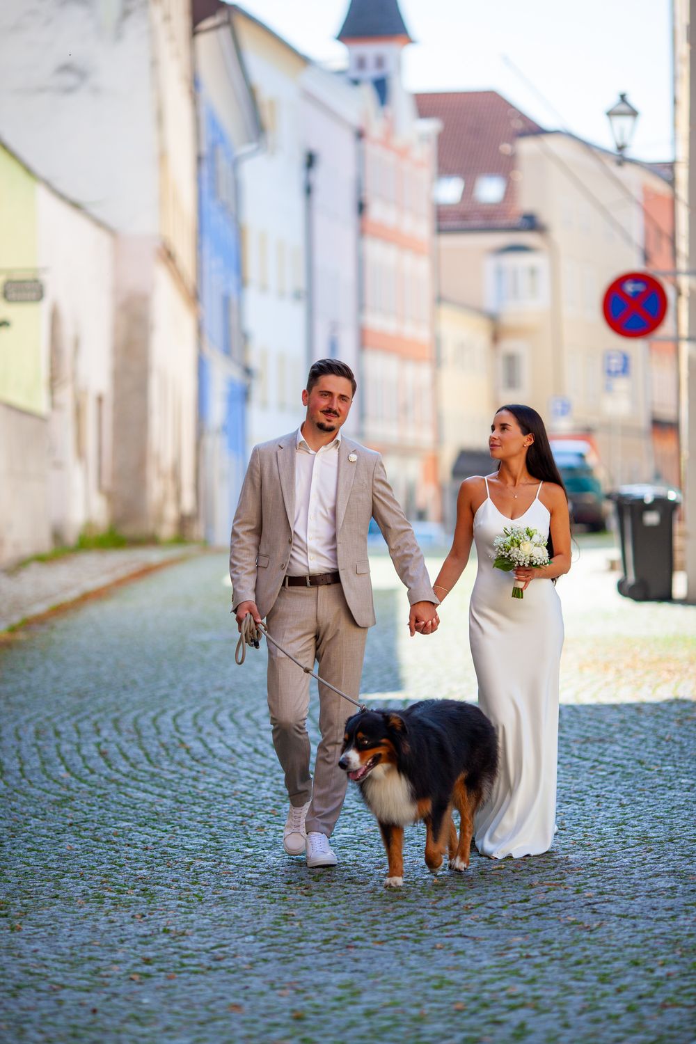 A couple and their dog walk along a charming cobblestone street on their wedding day.