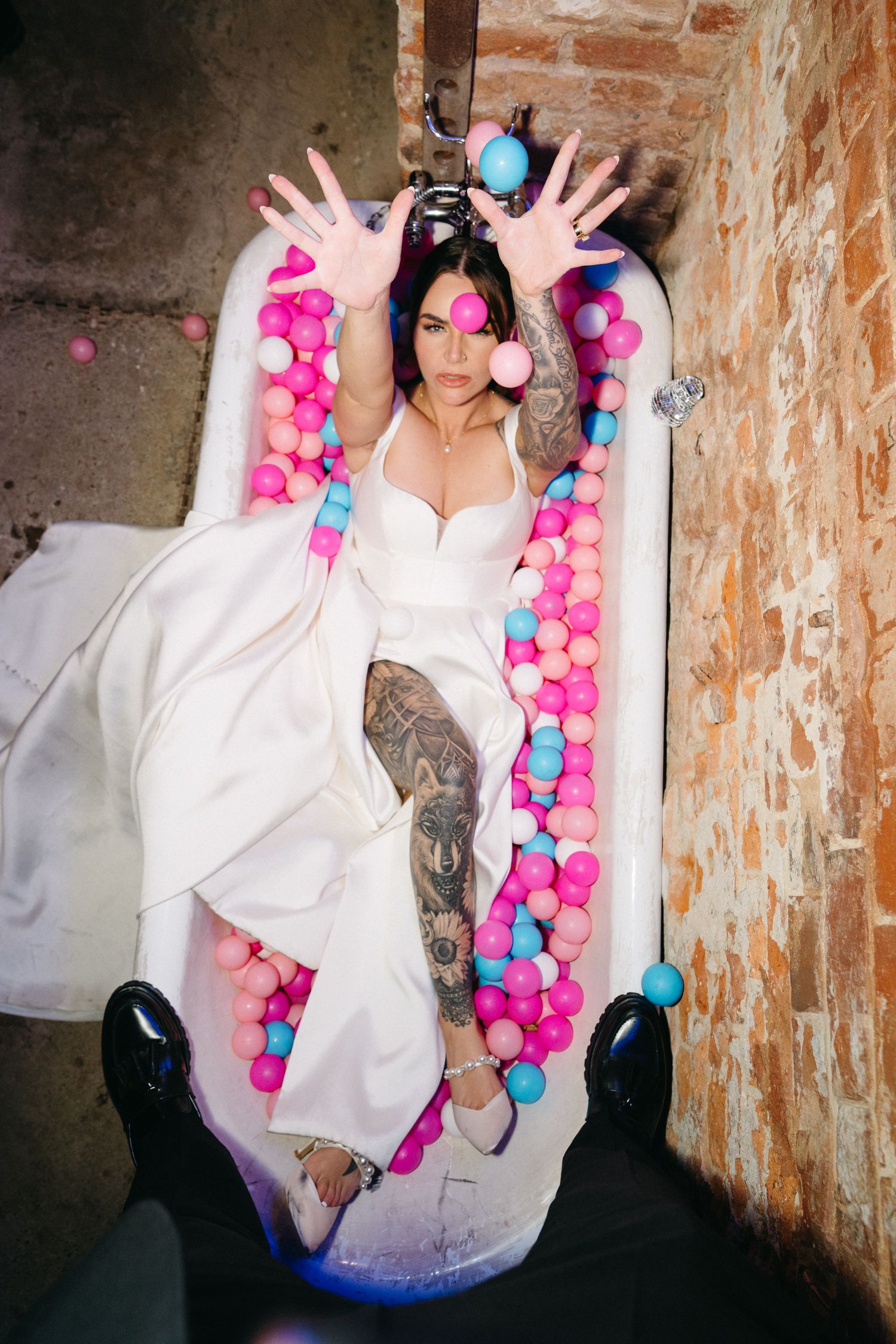 A creative bathtub photoshoot with colorful pink and blue balloon decorations against exposed brick walls.
