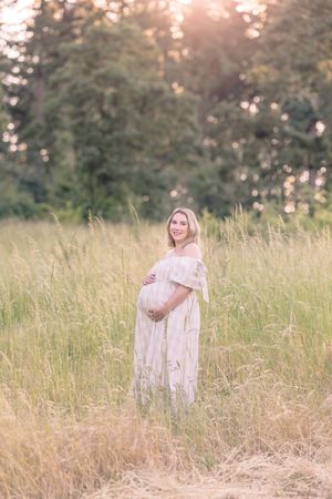 Woman in a flowy dress stands in a tall grass field at sunset.