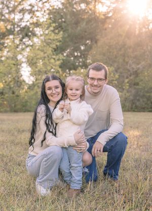 A family sits together in a sunlit grassy field during golden hour.