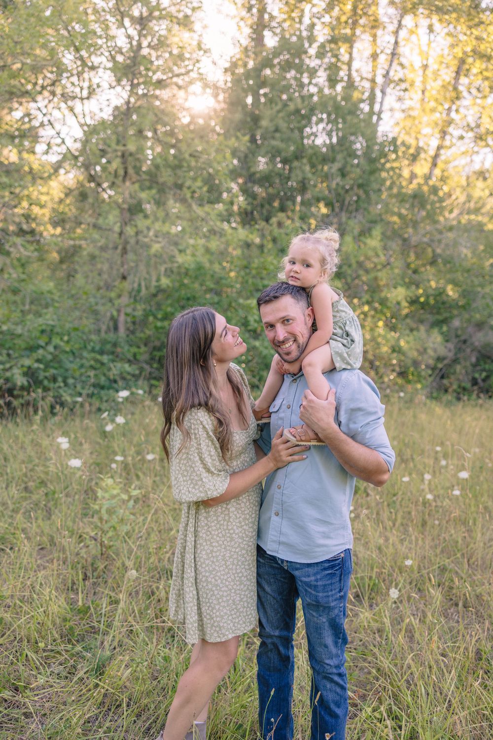 Playful couple laughing together in a sunlit meadow during golden hour.