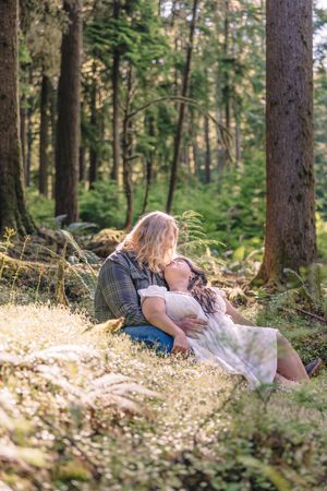 Couple lying in a wooded forest area surrounded by ferns and pine trees.