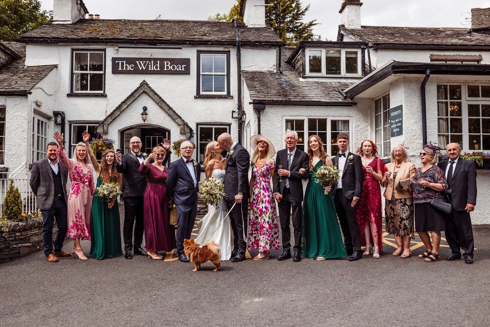 Wedding party guests pose for group photos outside a traditional English pub with white exterior walls and dark trim.