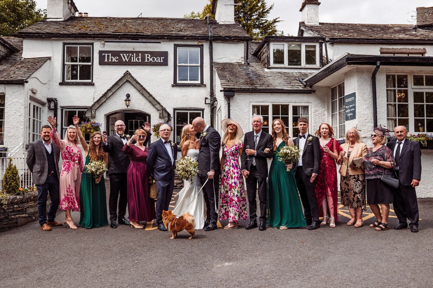 Wedding party guests pose for group photos outside a traditional English pub with white exterior walls and dark trim.